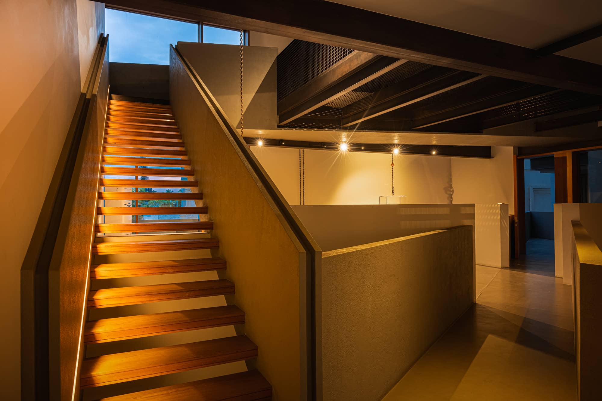 Staircase with timber treads rising beside a white partition wall — after dark