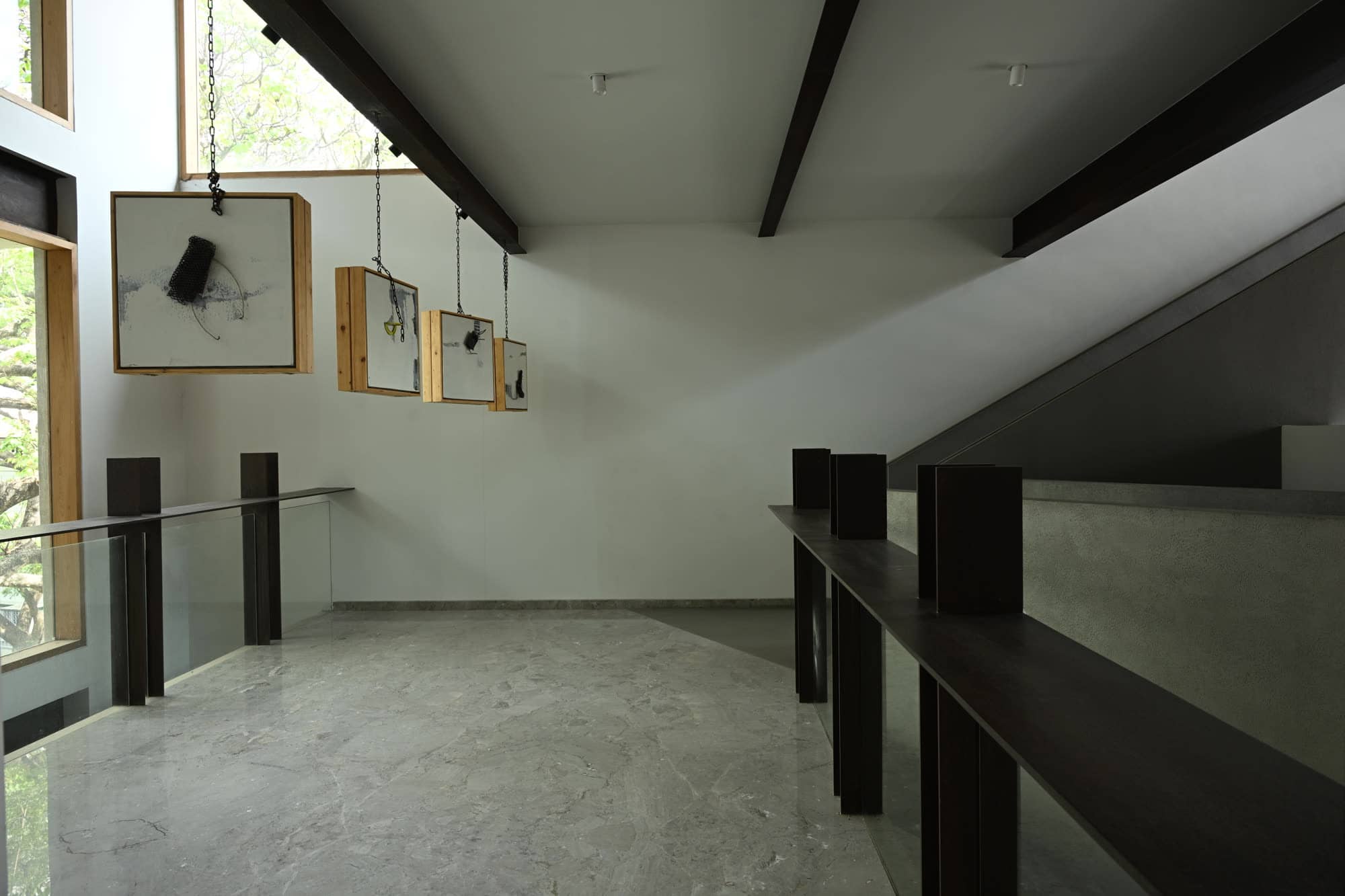 Gallery landing beneath a sloped white ceiling, with framed works along the wall and a steel railing — daylight
