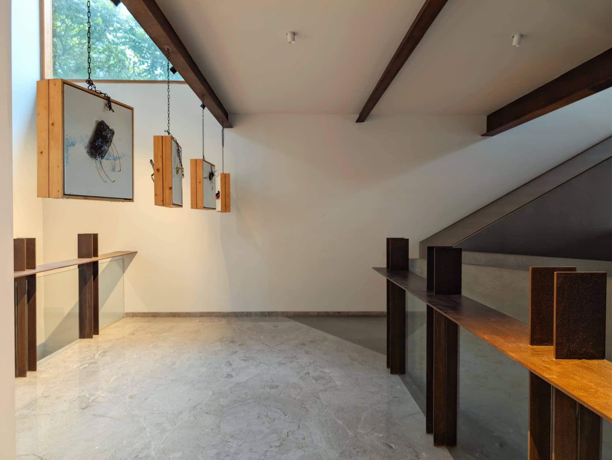 Gallery landing beneath a sloped white ceiling, with framed works along the wall and a steel railing — after dark