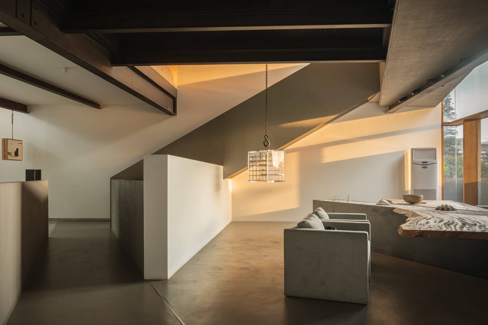 Sloped-ceiling lounge with a freestanding white partition, armchairs, and a sculptural bench — daylight