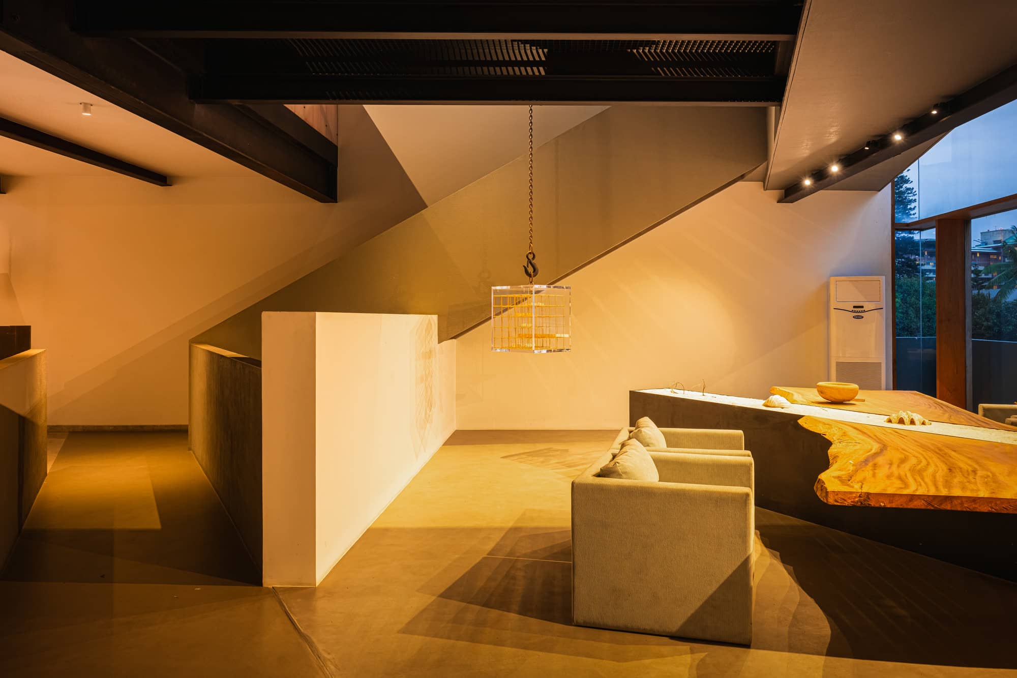 Sloped-ceiling lounge with a freestanding white partition, armchairs, and a sculptural bench — after dark