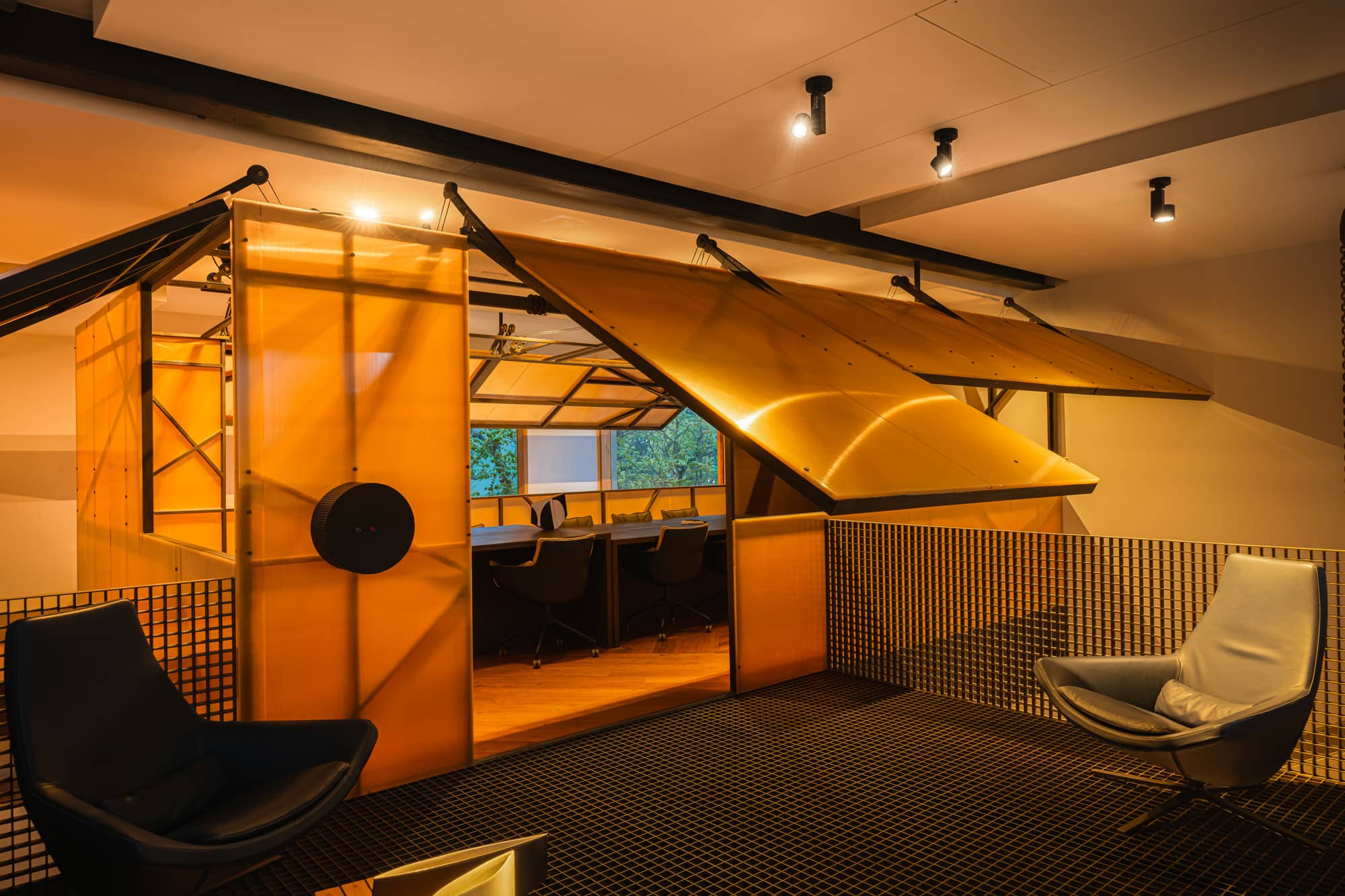 Folded plywood canopy panels suspended over a workspace, with lounge chairs in the foreground — after dark