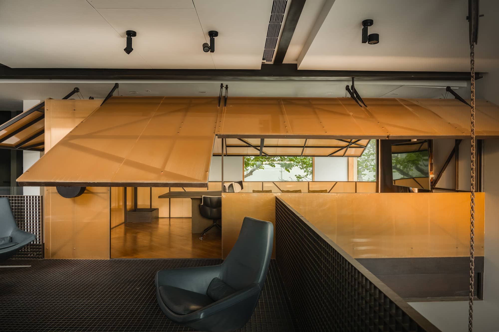 Timber-lined studio behind a mesh railing, with a suspended plywood canopy and a lounge chair — daylight