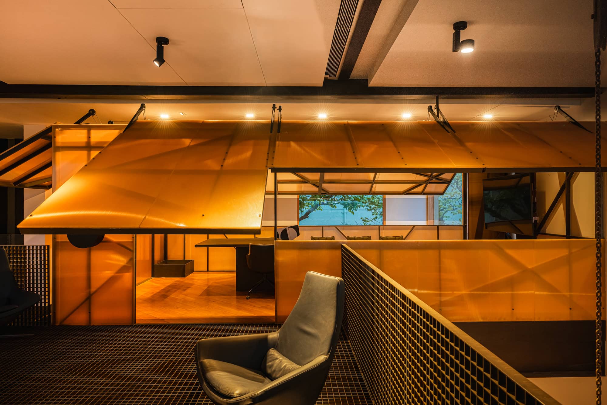 Timber-lined studio behind a mesh railing, with a suspended plywood canopy and a lounge chair — after dark