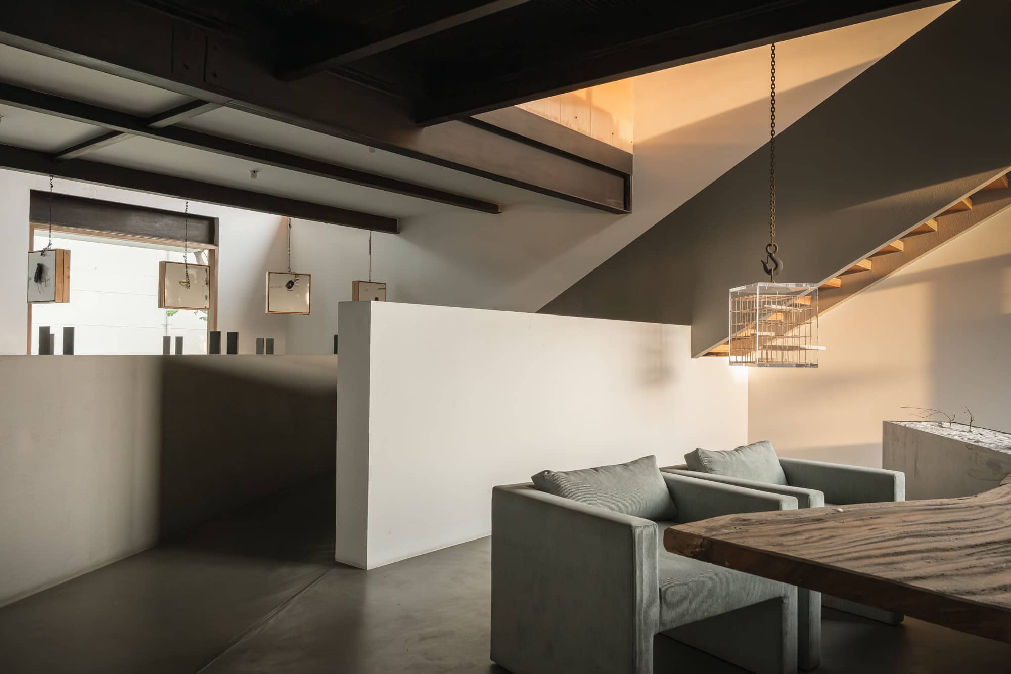 Lounge beneath exposed sloped beams, with a white partition, armchairs, and a timber table — daylight
