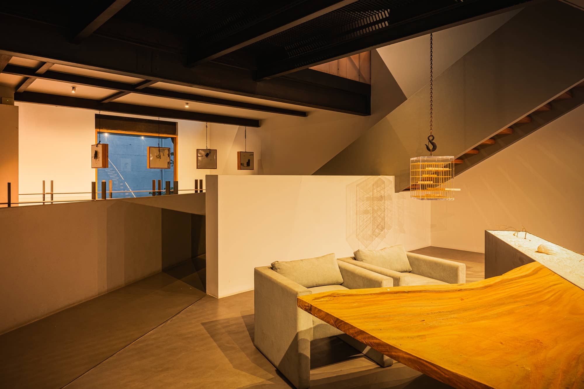 Lounge beneath exposed sloped beams, with a white partition, armchairs, and a timber table — after dark
